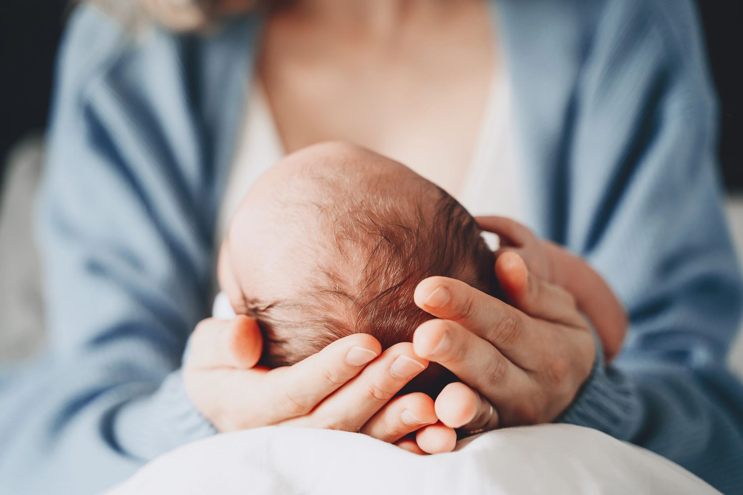 A person gently cradling a newborn baby's head in their hands.