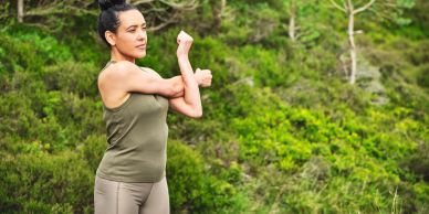Woman stretching outdoors in a green natural setting.