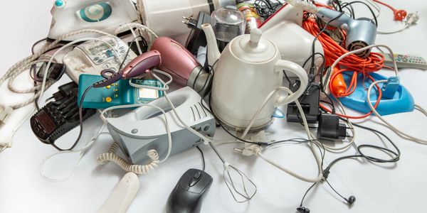 A pile of various old electrical appliances and tangled cords on a white surface.