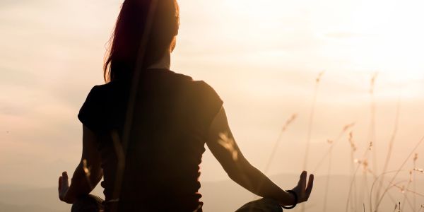 A person meditating outdoors during sunset.