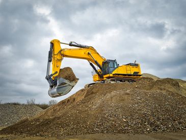 Excavator digging a pile of dirt under a cloudy sky.