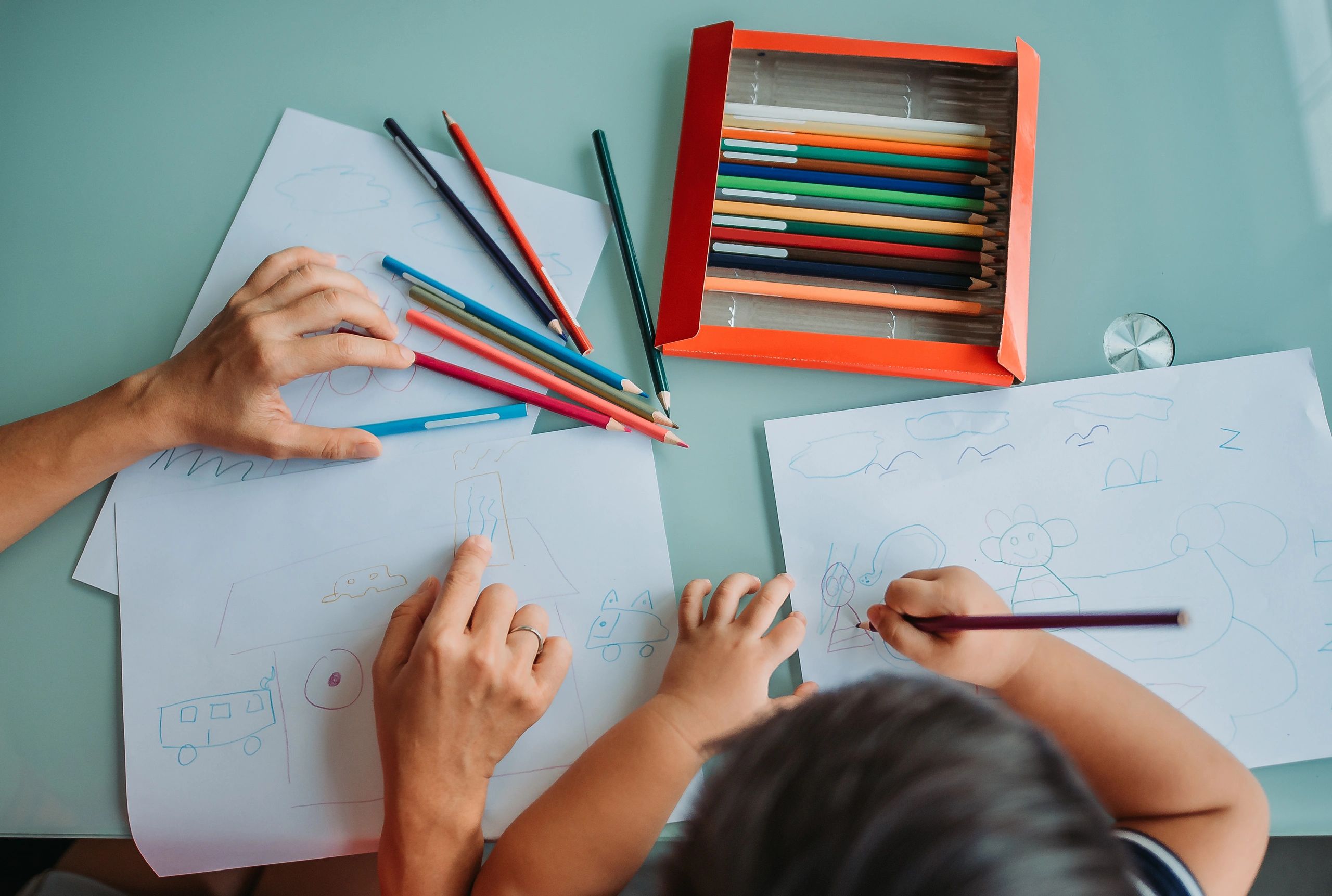 Adult and child drawing colorful doodles together using colored pencils.