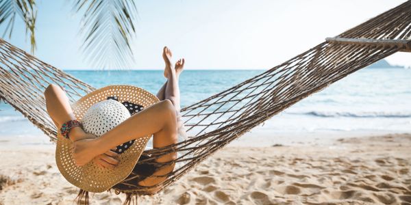 Person relaxing in a hammock on a sunny beach.