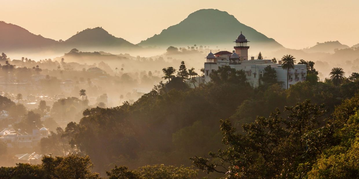 Misty morning with a palace on a hill surrounded by trees and mountains.