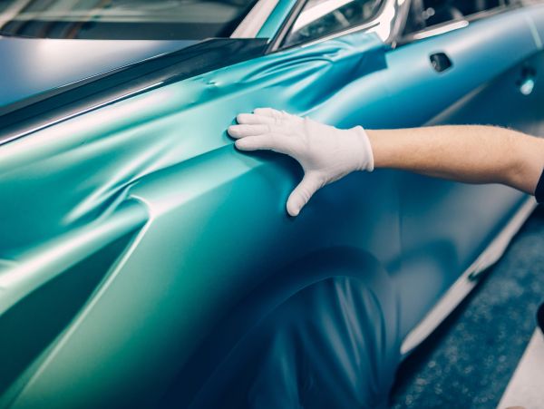 Person applying teal vinyl wrap to a car.