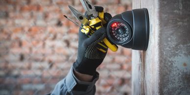 Hand holding tools near a security camera on a wall.