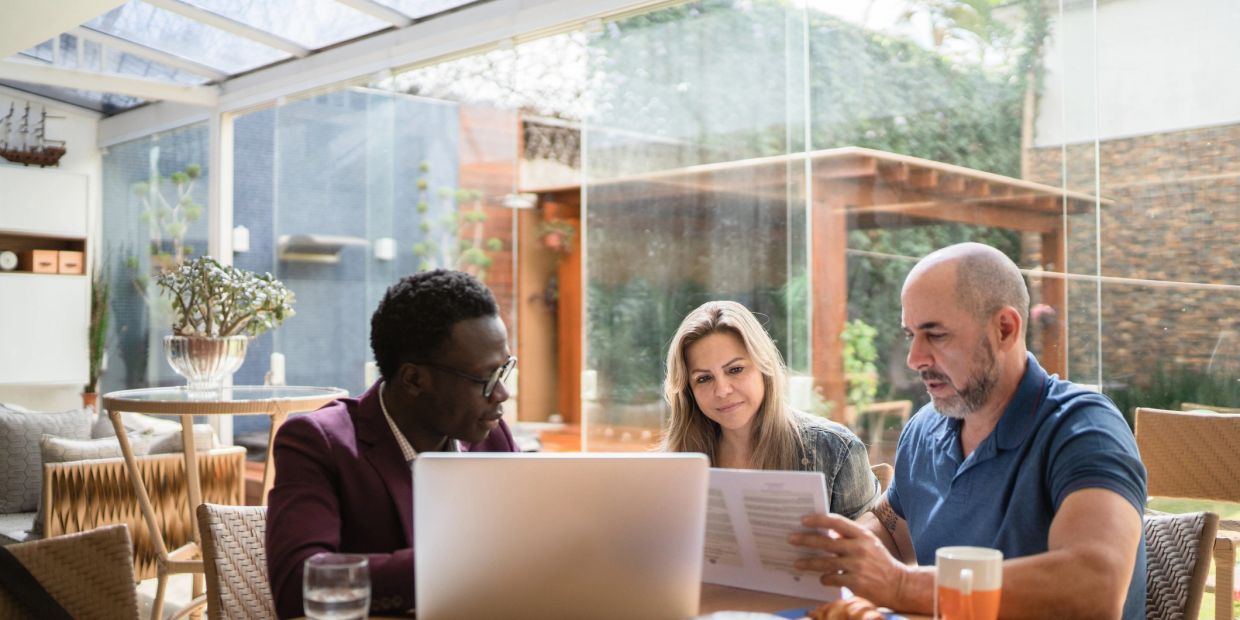 Three people having a discussion with documents and laptop.