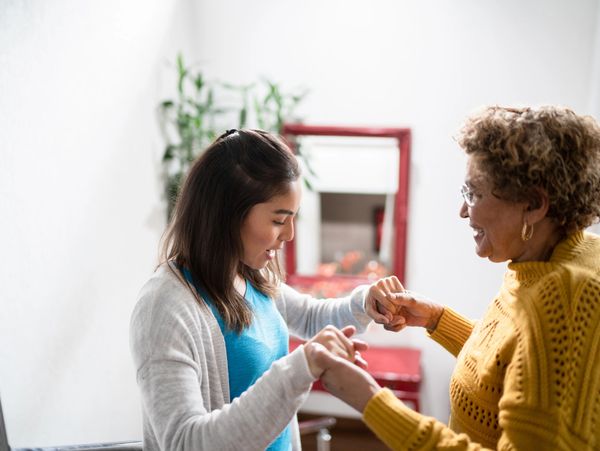 Young woman and elderly woman holding hands joyfully indoors.