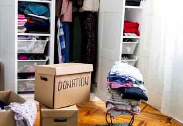 A donation box with folded clothes and an open wardrobe in the background.