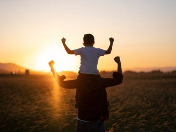 Child on shoulders at sunset.
