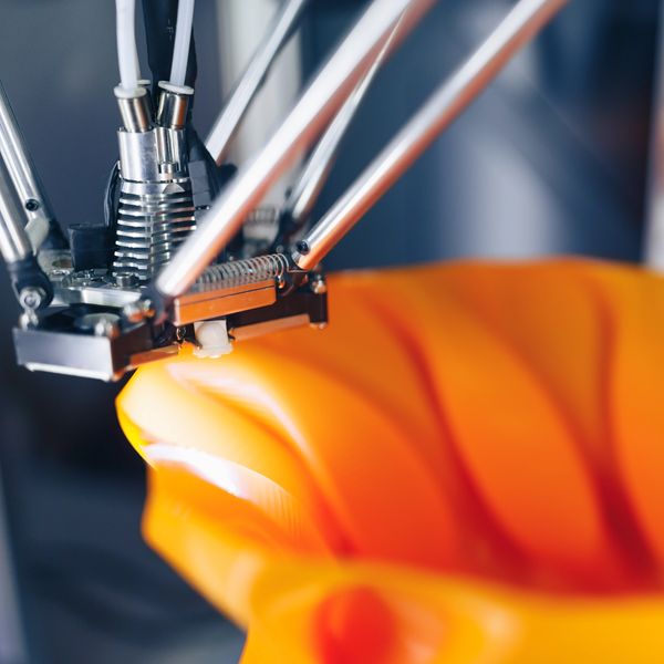 Close-up of a 3D printer nozzle shaping an orange object.