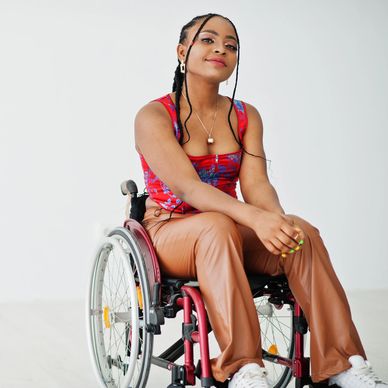 Black woman with long black braids sitting in red wheelchair smiling 