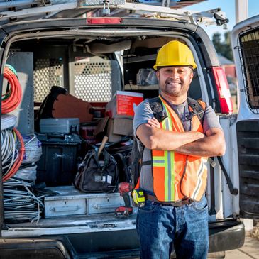 Smiling construction worker with safety gear standing by a work van.