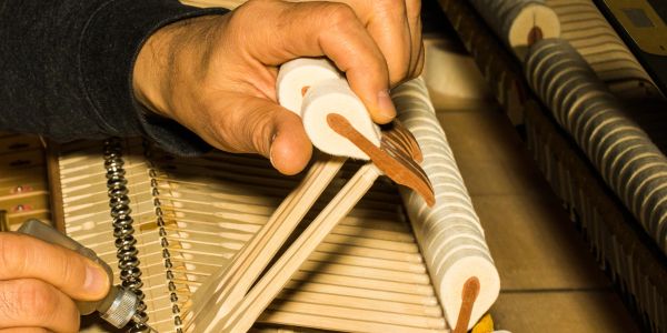 Hands tuning piano strings with a tool.