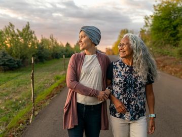 Two women smiling and walking arm in arm outdoors at sunset.
