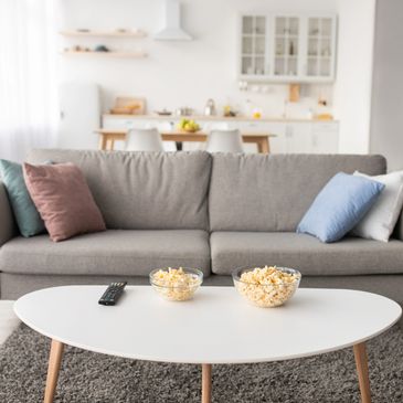 Modern living room with gray sofa, colorful pillows, and popcorn on white coffee table.