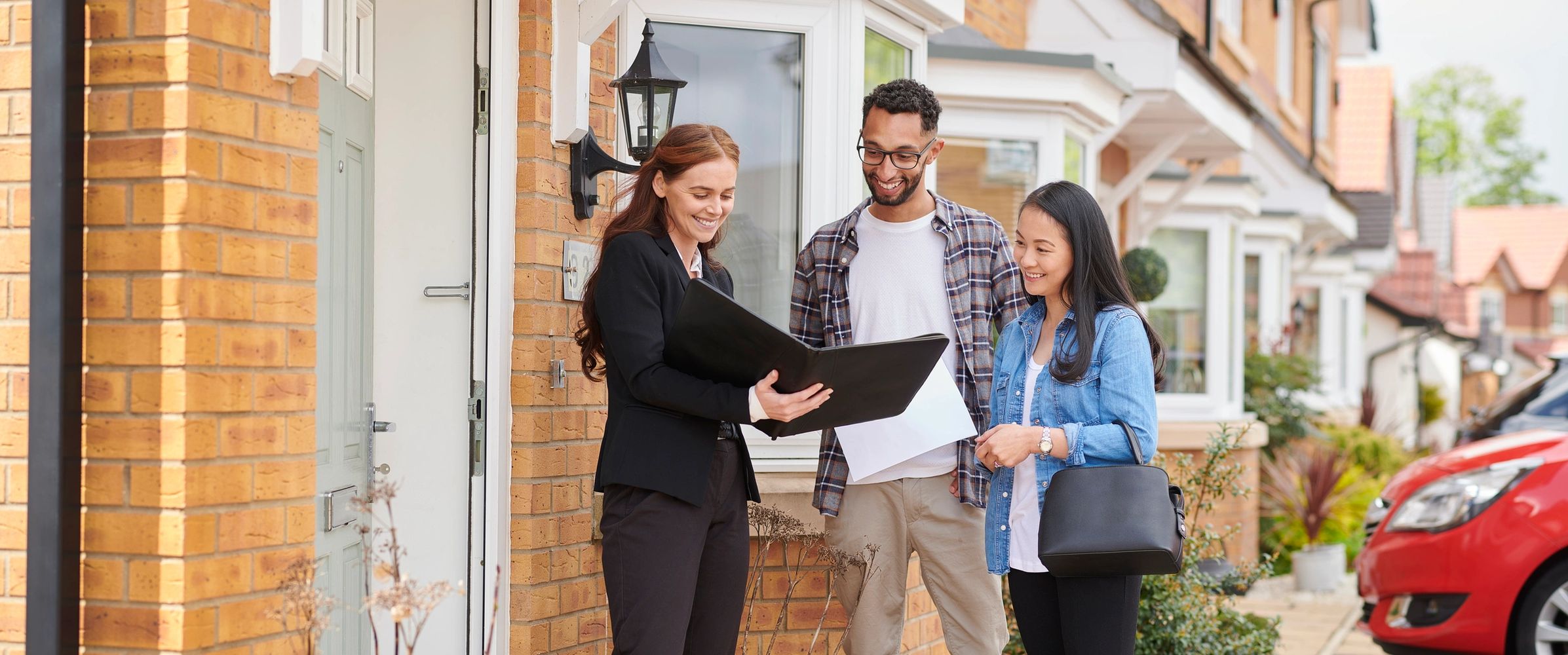 Realtor showing a couple a property document outside a house.