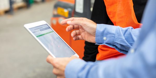 Two workers reviewing data on a tablet in a warehouse setting.