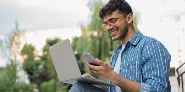 Man using laptop and phone outdoors.