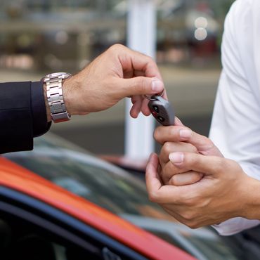 Two people exchanging car keys near a red vehicle.