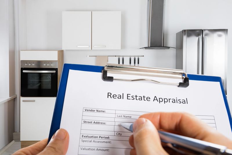 Close-up Of Person Hand Filling Real Estate Appraisal Document In Front Of House