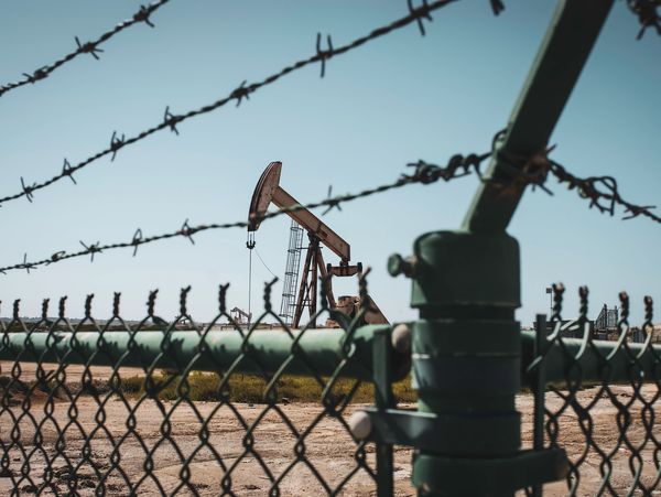 Oil pump behind a barbed wire fence under clear sky.
