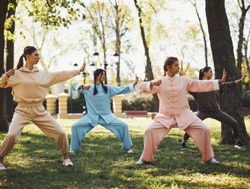 Four women practicing Tai Chi in a park on a sunny day.