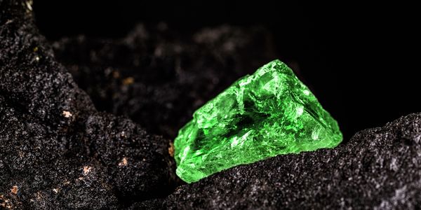A vibrant green crystal resting on dark volcanic rocks.