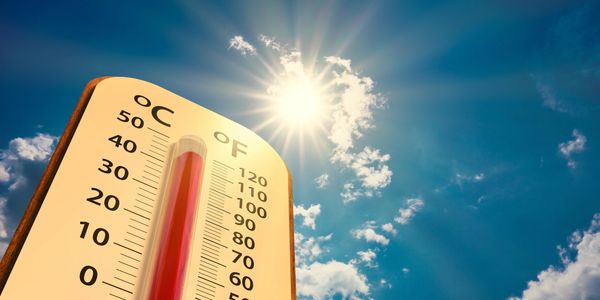 Thermometer showing high temperature under bright sun and blue sky.