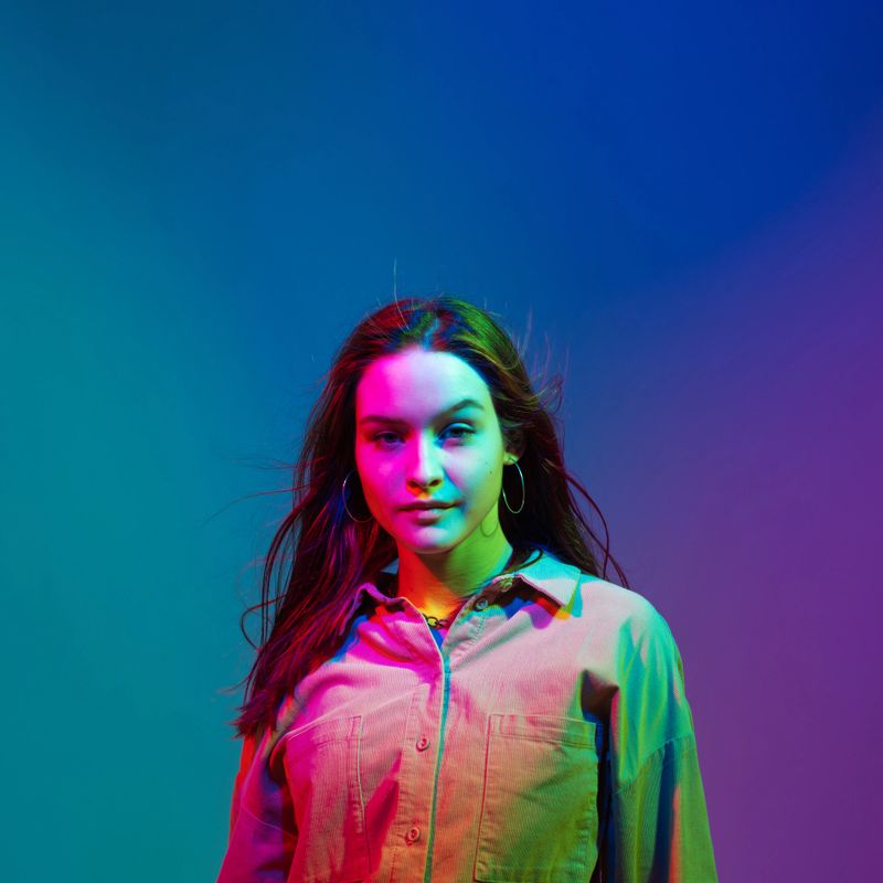 Confident yong stylish modern girl with long waving hair posing in colourful neon studio light. Woman beauty portrait. High quality photo