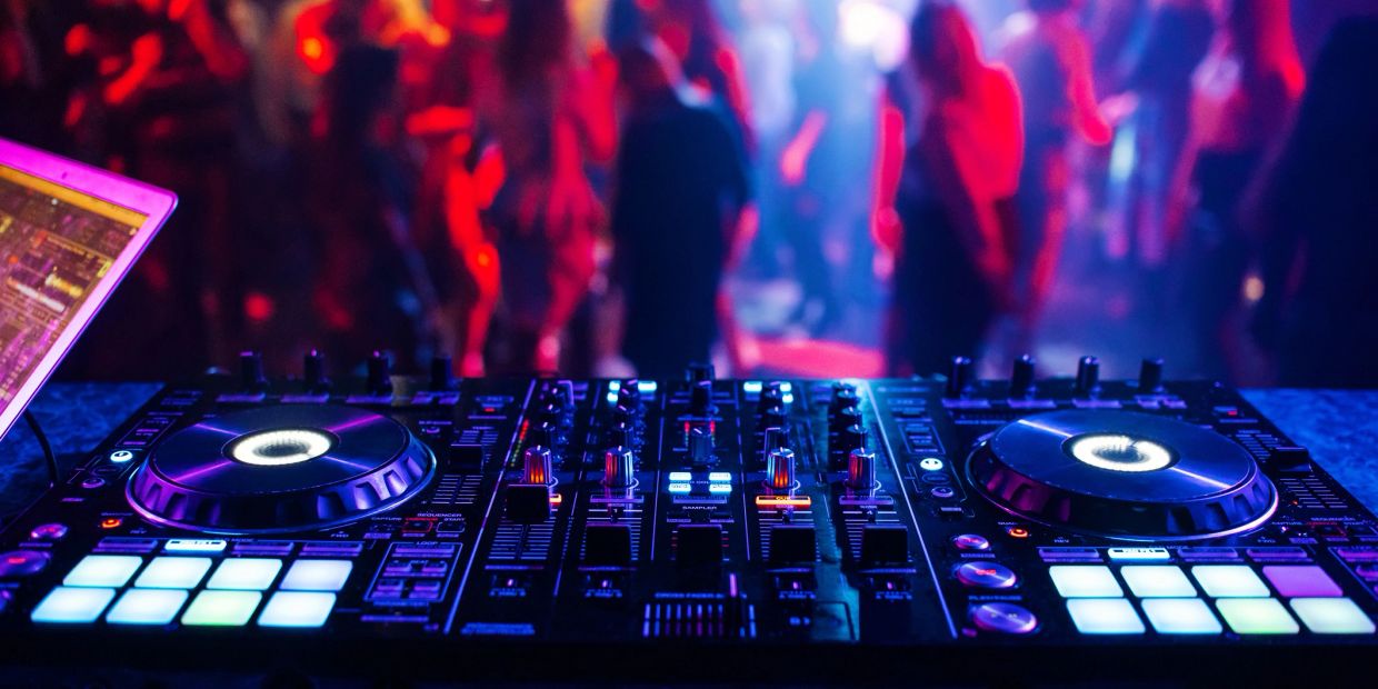 Consola de DJ en club con luces y gente.