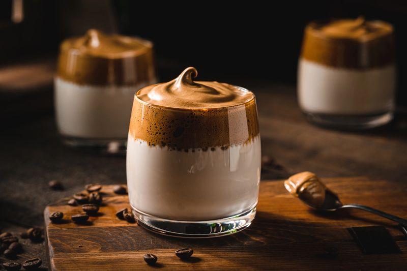 Homemade trendy Dalgona coffee on wooden table with a spoon of sweet foam. Dalgona coffee with coffee beans on table.