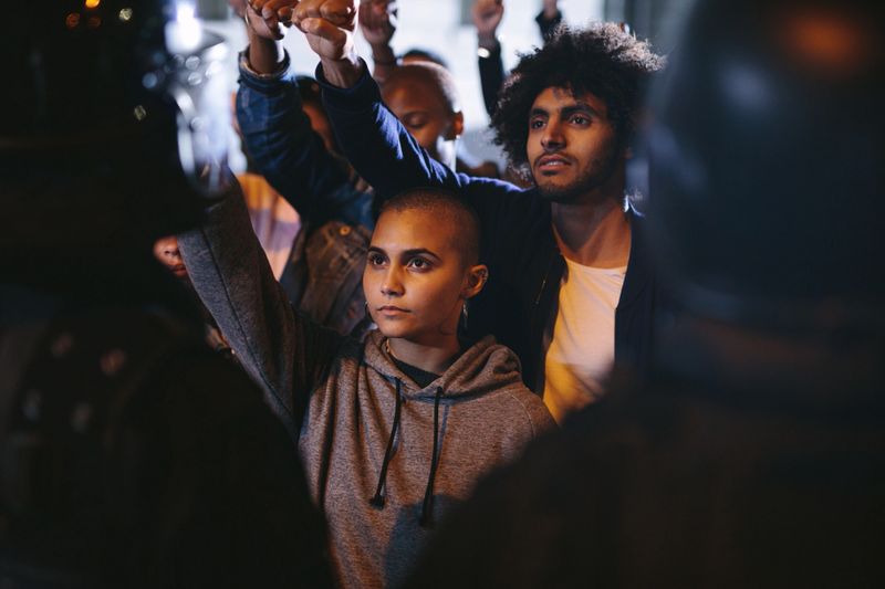 Group of furious protestors giving slogans in front of police force. Group of men and women demonstrating against police violence at night.