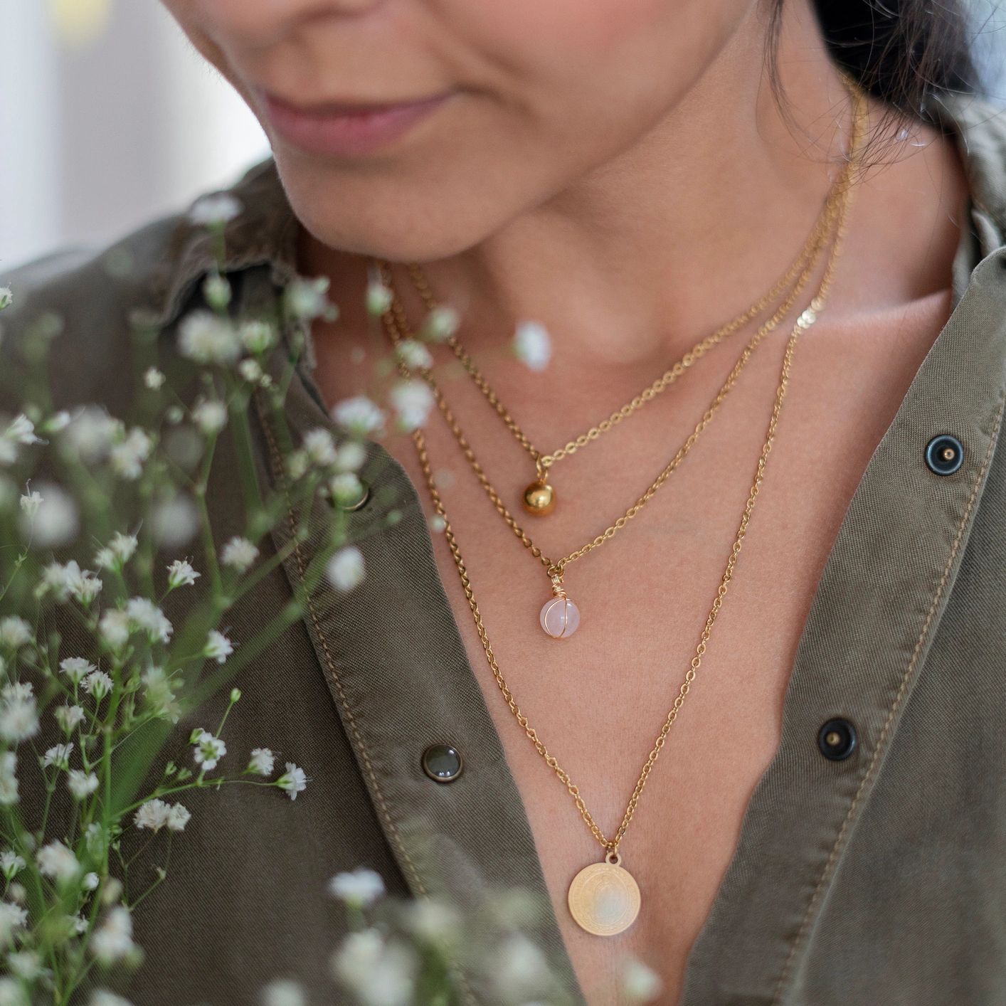 A woman wearing gold necklaces stands next to baby's breath white flowers