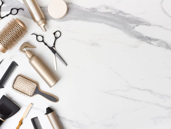 Hair styling tools and products arranged on a marble surface.