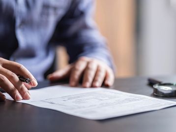 Person signing a document on a table with a pen.
