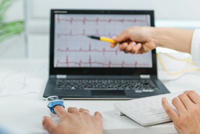 A doctor analyzing ECG results on a laptop while monitoring a patient's oxygen levels.