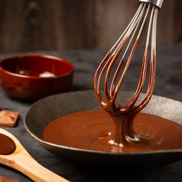 Whisk mixing smooth chocolate sauce in a dark bowl.