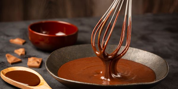 Whisking rich melted chocolate in a black bowl on a dark surface.