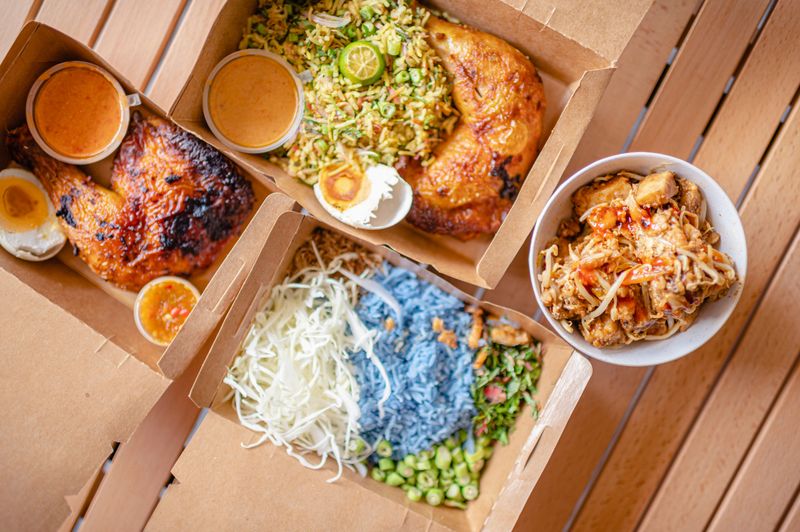 table top view malaysian food nasi kerabu, nasi ulam and ayam percik in recycled paper container with sauce