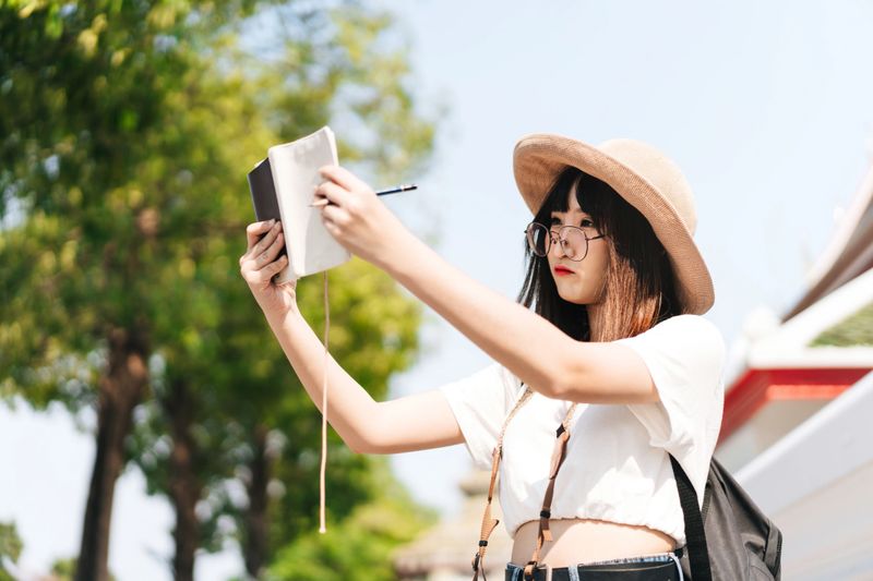 Young cute asian glasses girl traveller guide with journal list and thinking about plan trip. Sightseeing backpack on summer concept. People outdoor traveling in Bangkok, Thailand.