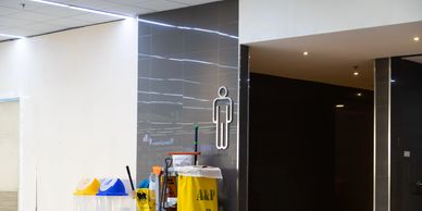 A hallway with a men's restroom sign, cleaning equipment, and recycling bins.