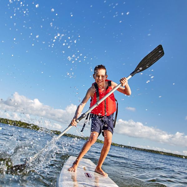 Boy paddleboarding on a lake, splashing water with his paddle.