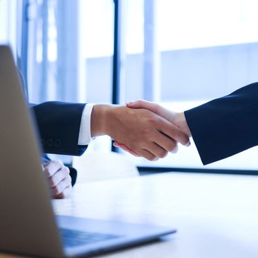 Uścisk dłoni między partnerami biznesowymi przy biurku – rozpoczęcie współpracy IT body leasing.