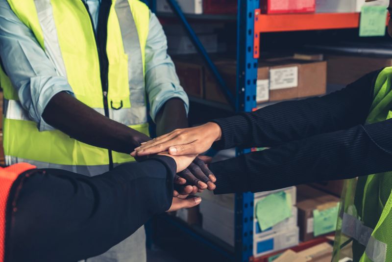 Factory workers stacking hands together in warehouse or storehouse . Logistics , supply chain and warehouse business concept .