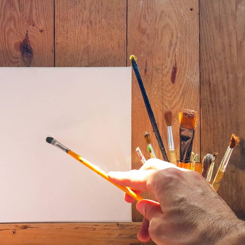 The artist's hand with a brush draws on the canvas. Creativity and inspiration. Intellectual work. Square photo.