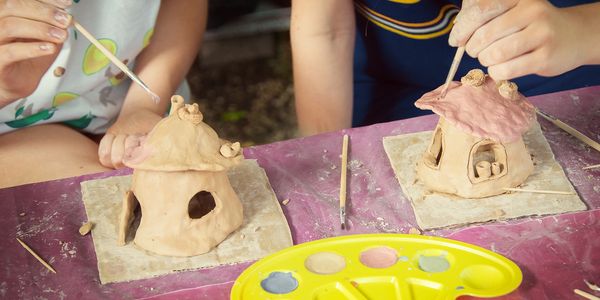 Children painting small clay houses with a paintbrush.