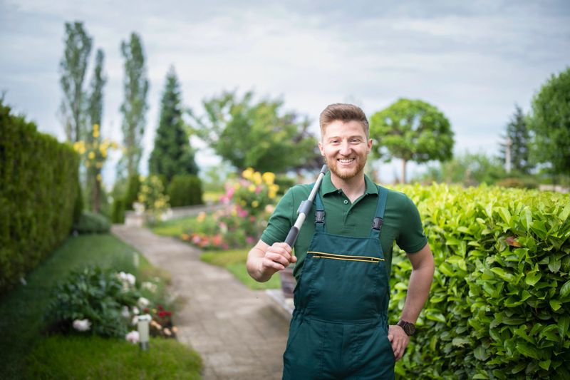 Portrait of smiling man in beautiful garden, holding trimming scissors and looking at camera, professional landscaper portrait with copy space.