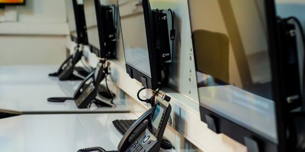 A row of telephones and monitors on a white desk in an office setting.