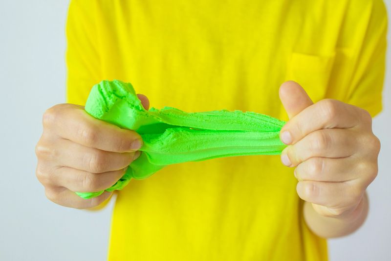 Hands with green slime close up. A child in a yellow t-shirt stretching slime. Trendy liquid toy sticks to hands. kids hands playing slime toy. soft dough milking children's games